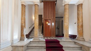 Μια επιβ λητική σκάλα με μαρμάρινες κολόνες και ένα κόκκινο χαλί που οδηγεί σε μια ξύλινη πόρτα.