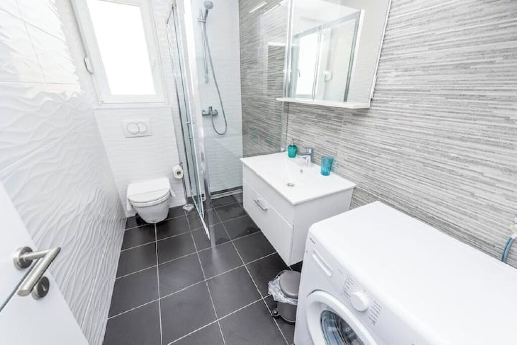 A modern bathroom with a toilet, shower, sink, and washing machine.