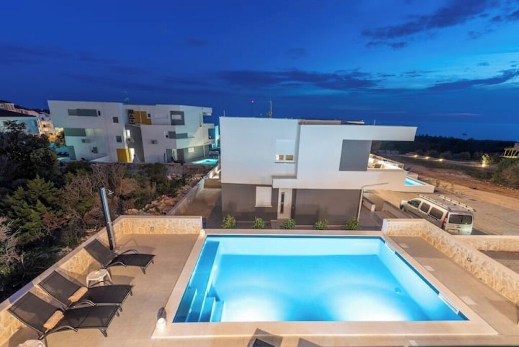 A modern house with a swimming pool, lounge chairs, and a view of other buildings.