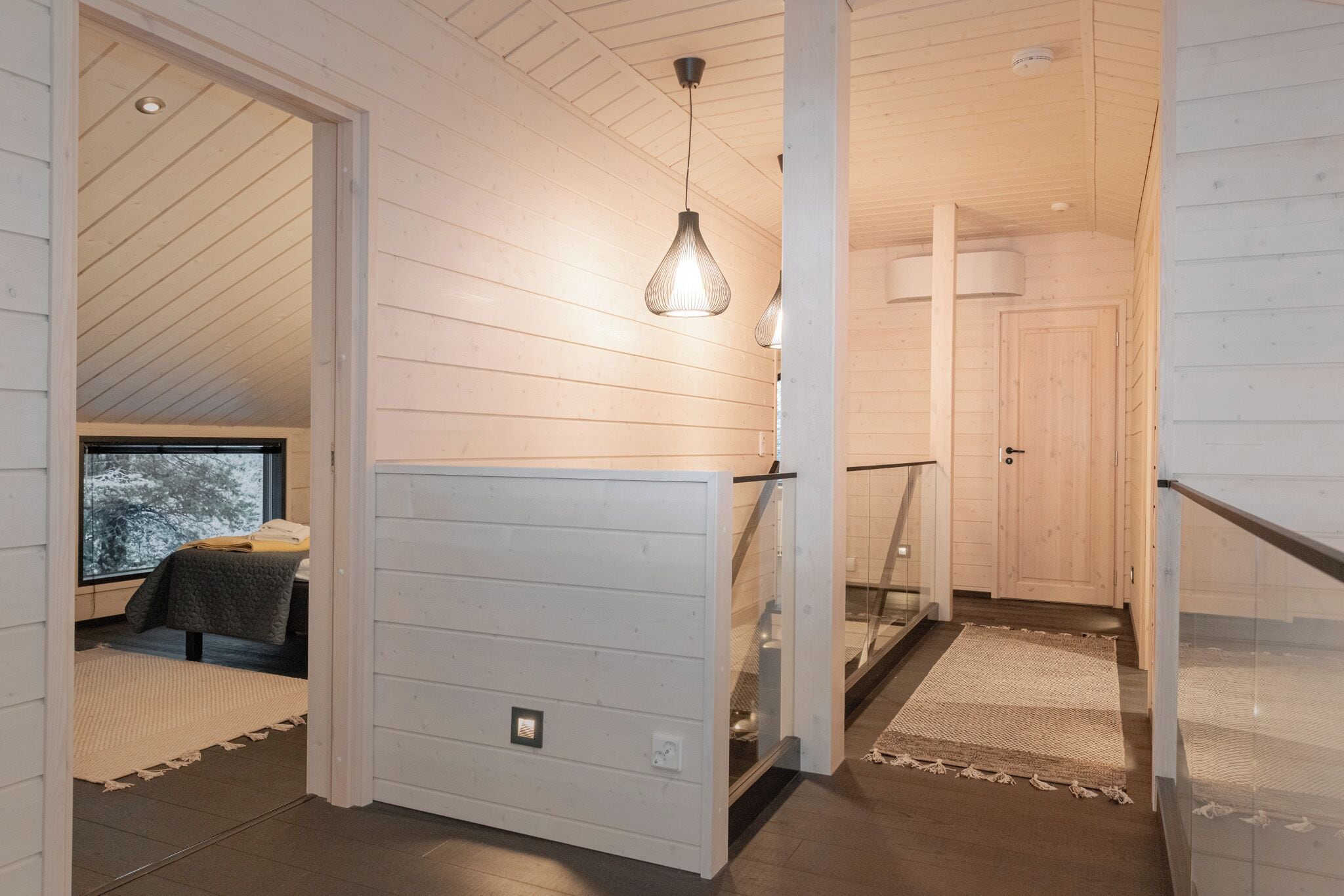 A wooden interior with a staircase, a hanging light fixture, and a view through a window.
