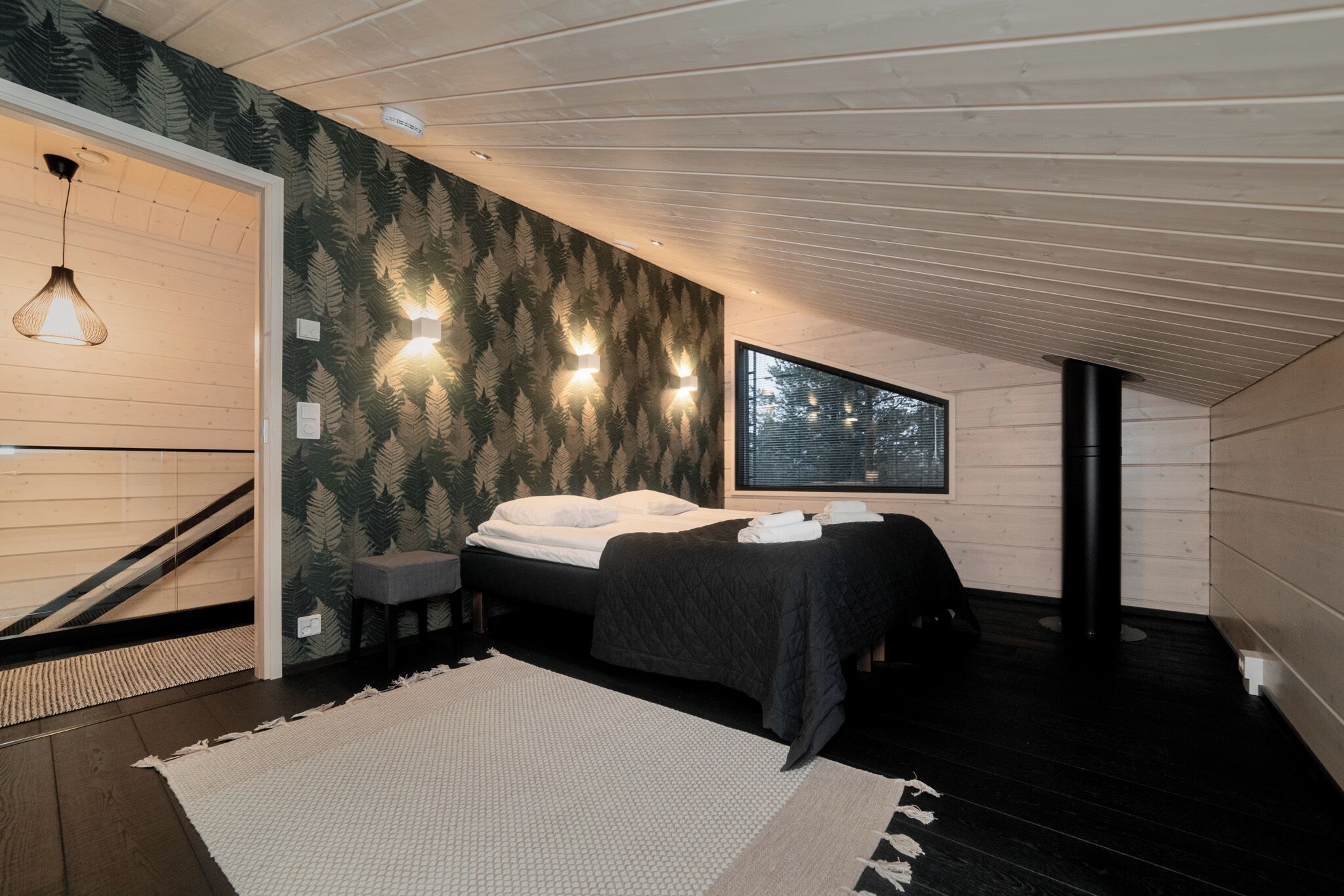 A modern bedroom with a bed, two bedside tables, a large window, and a wooden ceiling.