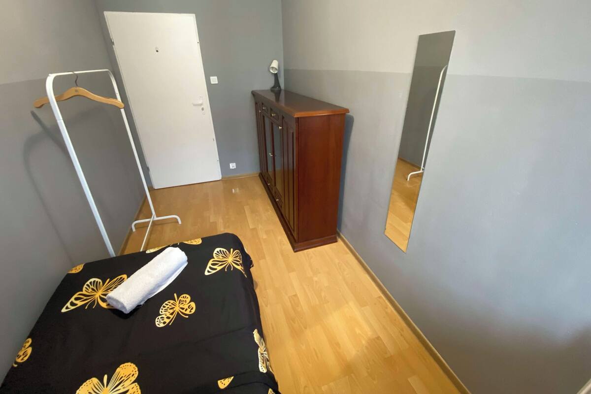 A bedroom with a bed, a wardrobe, a mirror, and a hanging clothes rack.