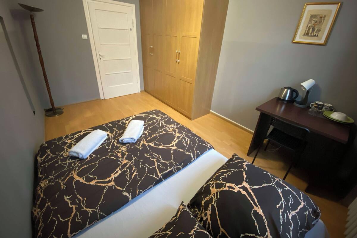 A bedroom with a bed, a wardrobe, a desk with a kettle, and a framed picture on the wall.