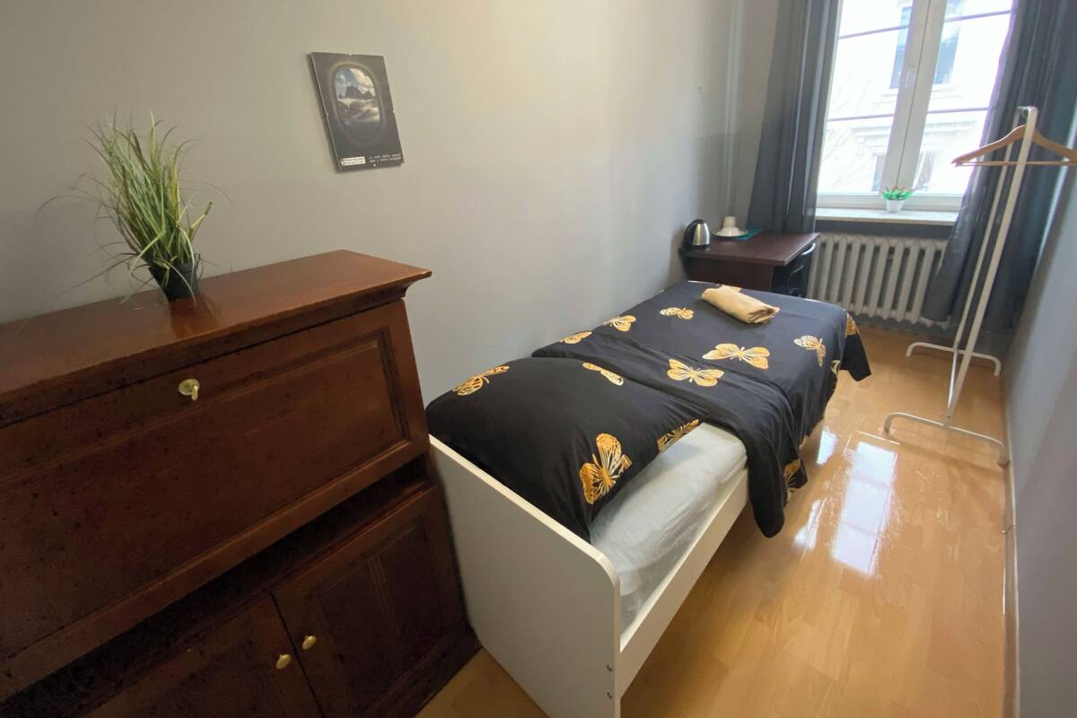 A bedroom with a bed, a dresser, a radiator, a window with curtains, and a small plant.