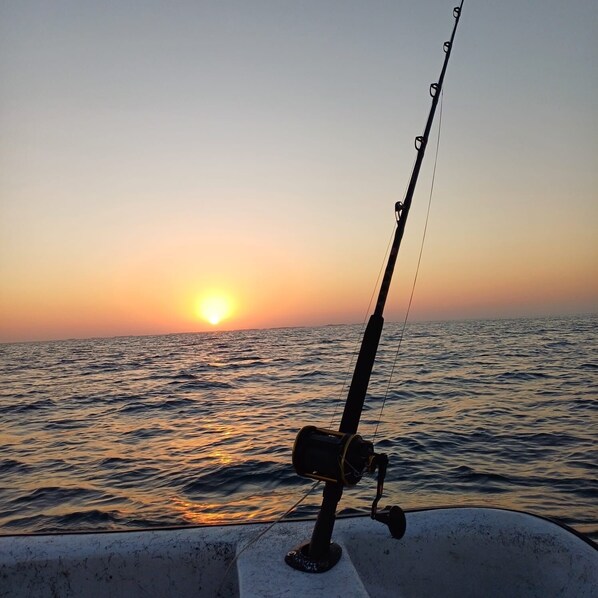 A fishing rod on a boat with the sun setting in the background. - Sunshine Cabanas At Ocean View (Dangriga)