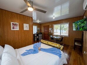 A hotel room with a bed, a ceiling fan, a dining area, and a television. - Sunshine Cabanas At Ocean View (Dangriga)
