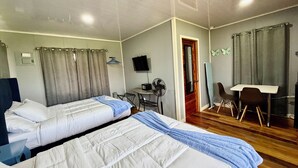 A hotel room with two beds, a desk, a chair, a TV, and a door. - Sunshine Cabanas At Ocean View (Dangriga)
