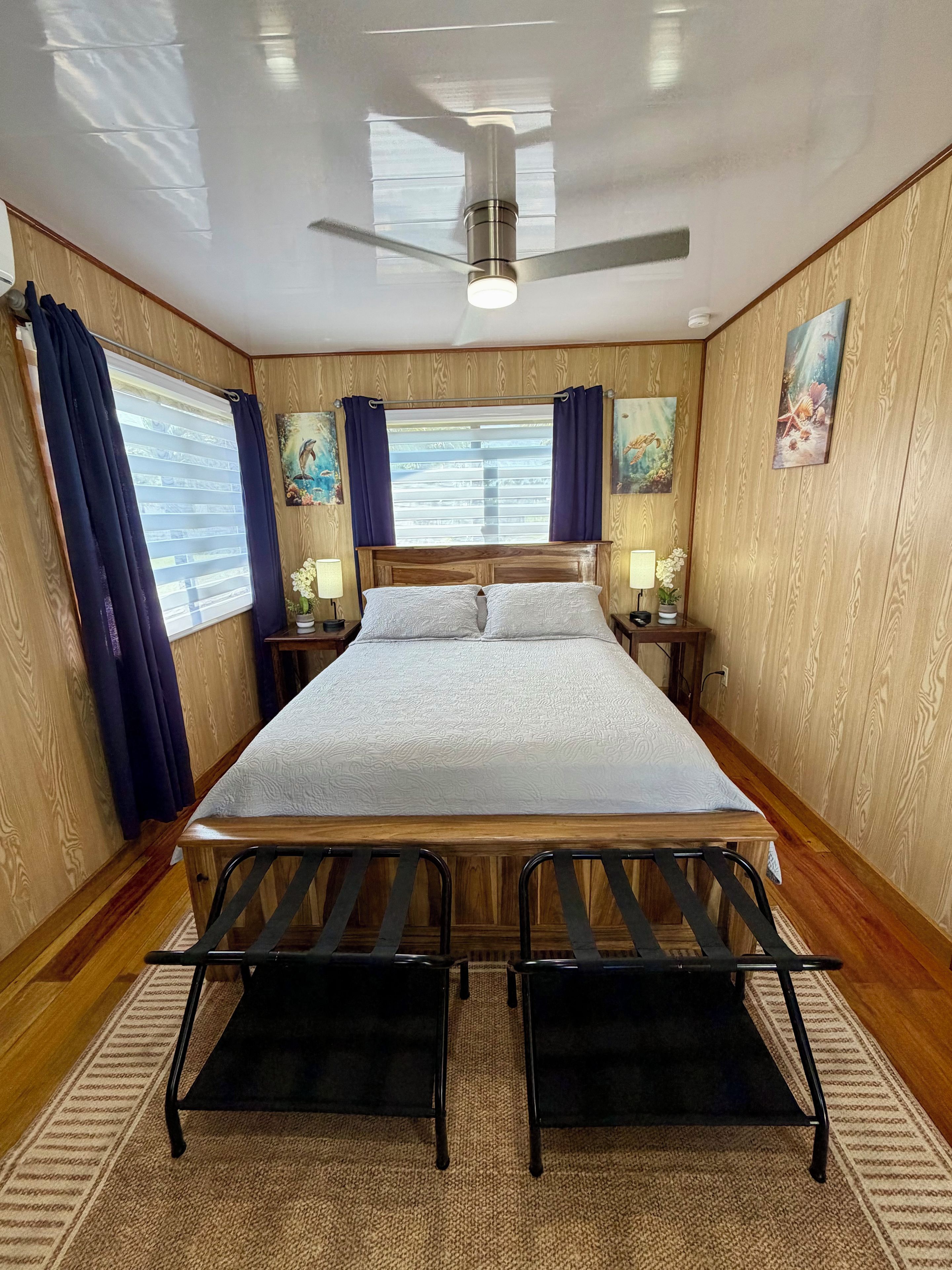 A hotel room with a bed, two nightstands, a ceiling fan, and a window with curtains.