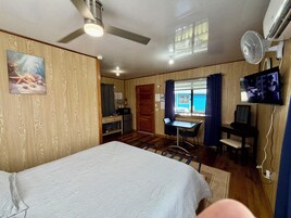 Una habitación con cama, escritorio, silla, televisor y ventilador de techo.