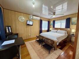 Una habitación de hotel con cama, escritorio, silla, televisor, ventilador de techo y paredes de madera.