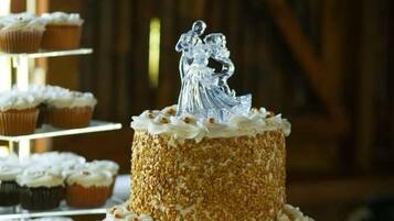 Un pastel de bodas con cobertura blanca y un adorno plateado, rodeado de cupcakes sobre una mesa.