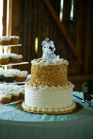 Un pastel de bodas con cobertura blanca y un adorno plateado, rodeado de cupcakes sobre una mesa.
