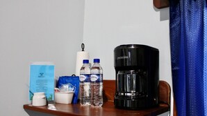 A small wooden table with a coffee maker, two water bottles, a cup, a tissue roll, and a blue bag. - Sunshine Cabanas At Ocean View (Dangriga)