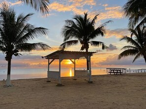 A beach with a gazebo, palm trees, and a sunset. - Sunshine Cabanas At Ocean View (Dangriga)