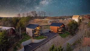 Two log cabin-style buildings with a central courtyard, surrounded by trees and a clear night sky. - Quiet Cabin Near Pkwy | Hot Tub | Game Room (Pigeon Forge)