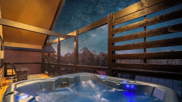 A hot tub with a wooden deck and a night sky view. - Quiet Cabin Near Pkwy | Hot Tub | Game Room (Pigeon Forge)