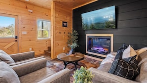A cozy living room with wooden walls, a fireplace, and comfortable seating. - Quiet Cabin Near Pkwy | Hot Tub | Game Room (Pigeon Forge)