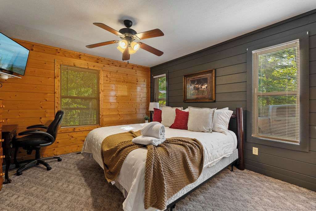 Un dormitorio con cama, ventilador de techo, televisión, escritorio y silla.