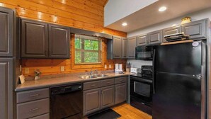 Una cocina con paredes de madera, armarios grises, un refrigerador negro y una ventana con persianas.