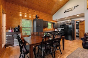 A wooden interior with a dining table and chairs, kitchen cabinets, and a refrigerator.