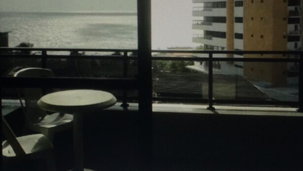 Un balcón con vista al mar y un edificio alto al fondo.