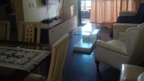 Una sala de estar con televisor, una mesa de comedor con sillas, un sofá y una ventana con cortinas.