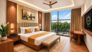 A modern hotel room with a large bed, a desk, a ceiling fan, and a view of the city. - Hotel Grand Shalimar by JMD Group (New Delhi)