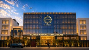 A modern hotel building with a prominent entrance, large windows, and a visible parking area. - Hotel Grand Shalimar by JMD Group (New Delhi)