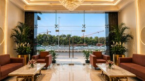 Eine Lobby mit einem Kronleuchter, Sofas, einem Marmortisch und großen Fenstern mit Blick auf Baukräne.