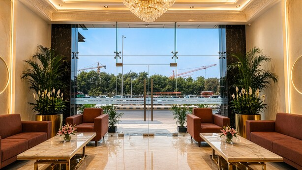 A lobby with a chandelier, sofas, a marble coffee table, and large windows with a view of construction cranes. - Hotel Grand Shalimar by JMD Group (New Delhi)