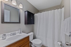 A bathroom with a white sink, a mirror with lights, a toilet, a shower curtain, and a towel rack. - Pet Friendly 4 Bedroom House in North Cape May (Lower Township)