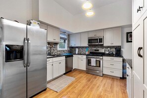 A modern kitchen with stainless steel appliances, white cabinetry, and a wooden floor. - Pet Friendly 4 Bedroom House in North Cape May (Lower Township)