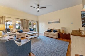 Un salon spacieux doté d’un ventilateur de plafond, de deux canapés, d’une table basse et offrant une vue sur l’extérieur grâce à de grandes fenêtres.