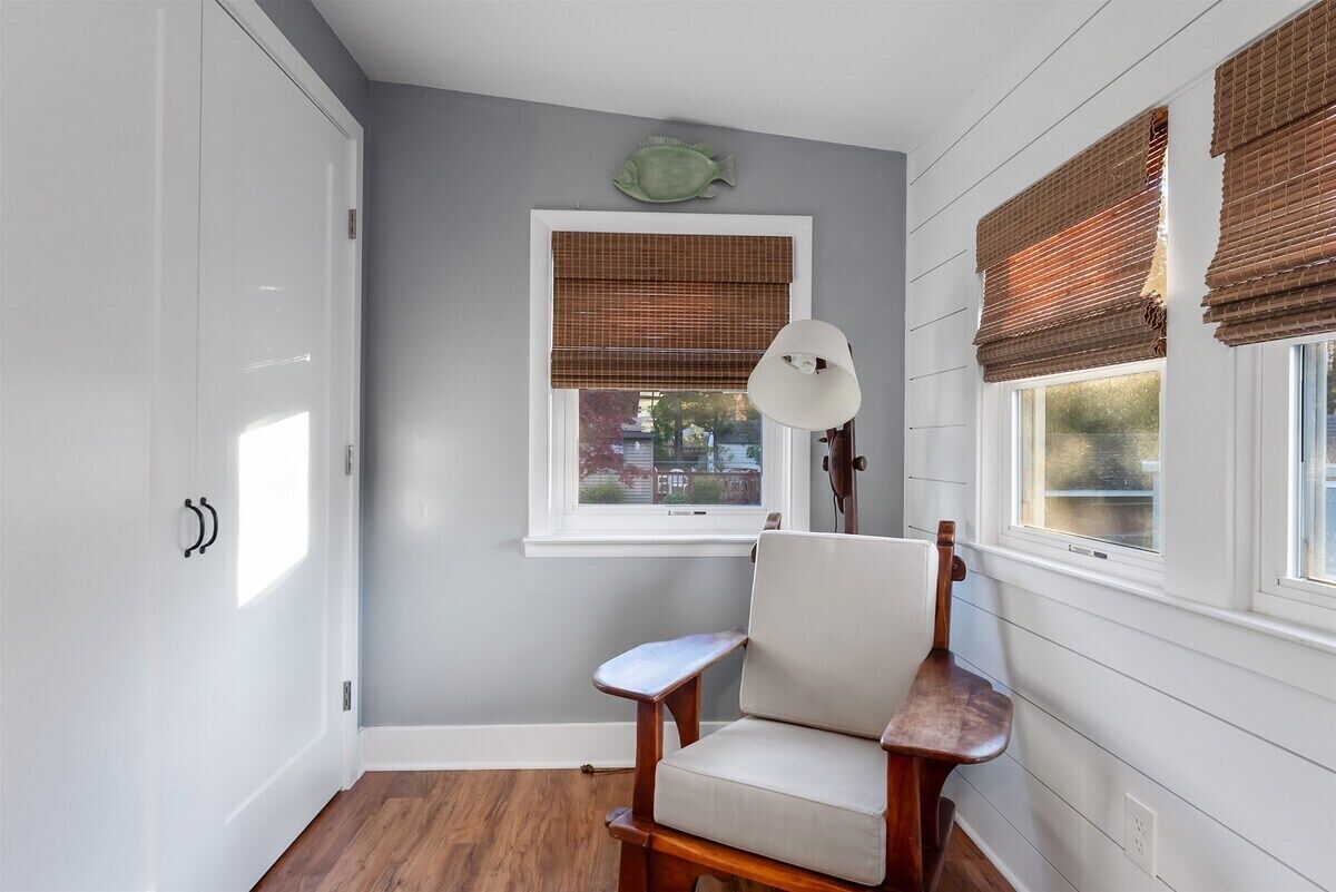 A room with a wooden chair, a white lamp, and a window with blinds.
