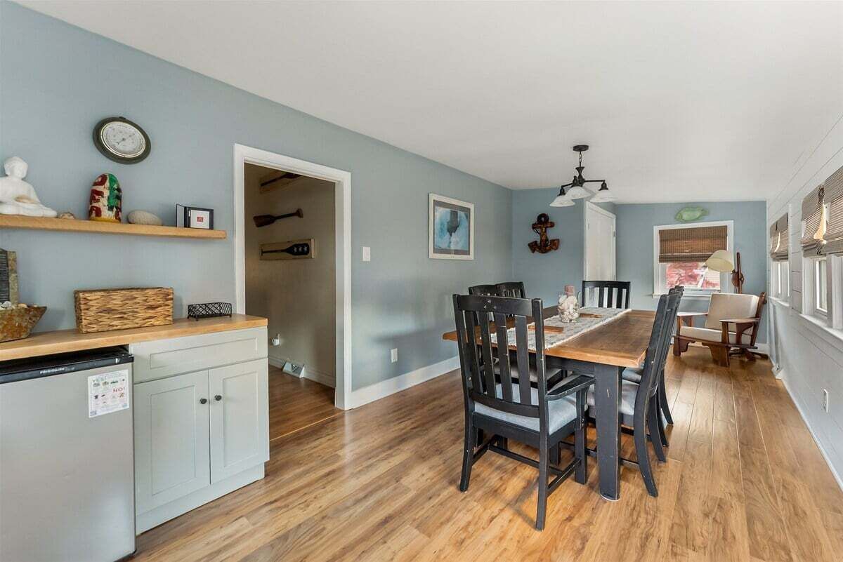 A dining area with a wooden table and chairs, a kitchen with a refrigerator and cabinets, and a hallway leading to another room.