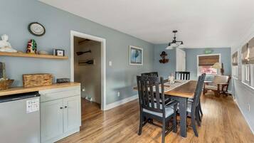 A dining area with a wooden table and chairs, a kitchen with a refrigerator and cabinets, and a hallway leading to another room.