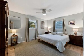 A bedroom with a bed, bedside lamps, a ceiling fan, and a window with curtains.