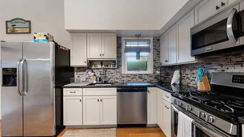 A modern kitchen with stainless steel appliances, white cabinetry, and a tiled backsplash.