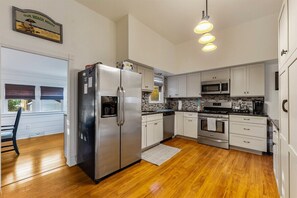 A modern kitchen with stainless steel appliances, white cabinetry, and a wooden floor.