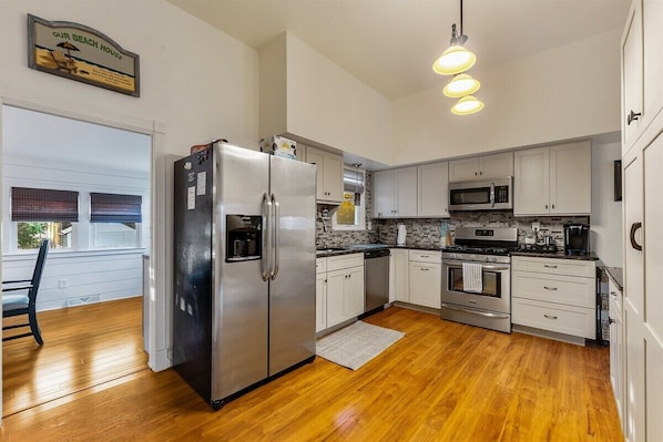 A modern kitchen with stainless steel appliances, white cabinetry, and a wooden floor.