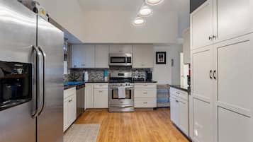 A modern kitchen with stainless steel appliances, white cabinetry, and a wooden floor.