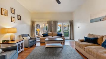 Un salon avec un canapé, une table basse et une lampe. Il y a un ventilateur de plafond et une fenêtre avec des rideaux.