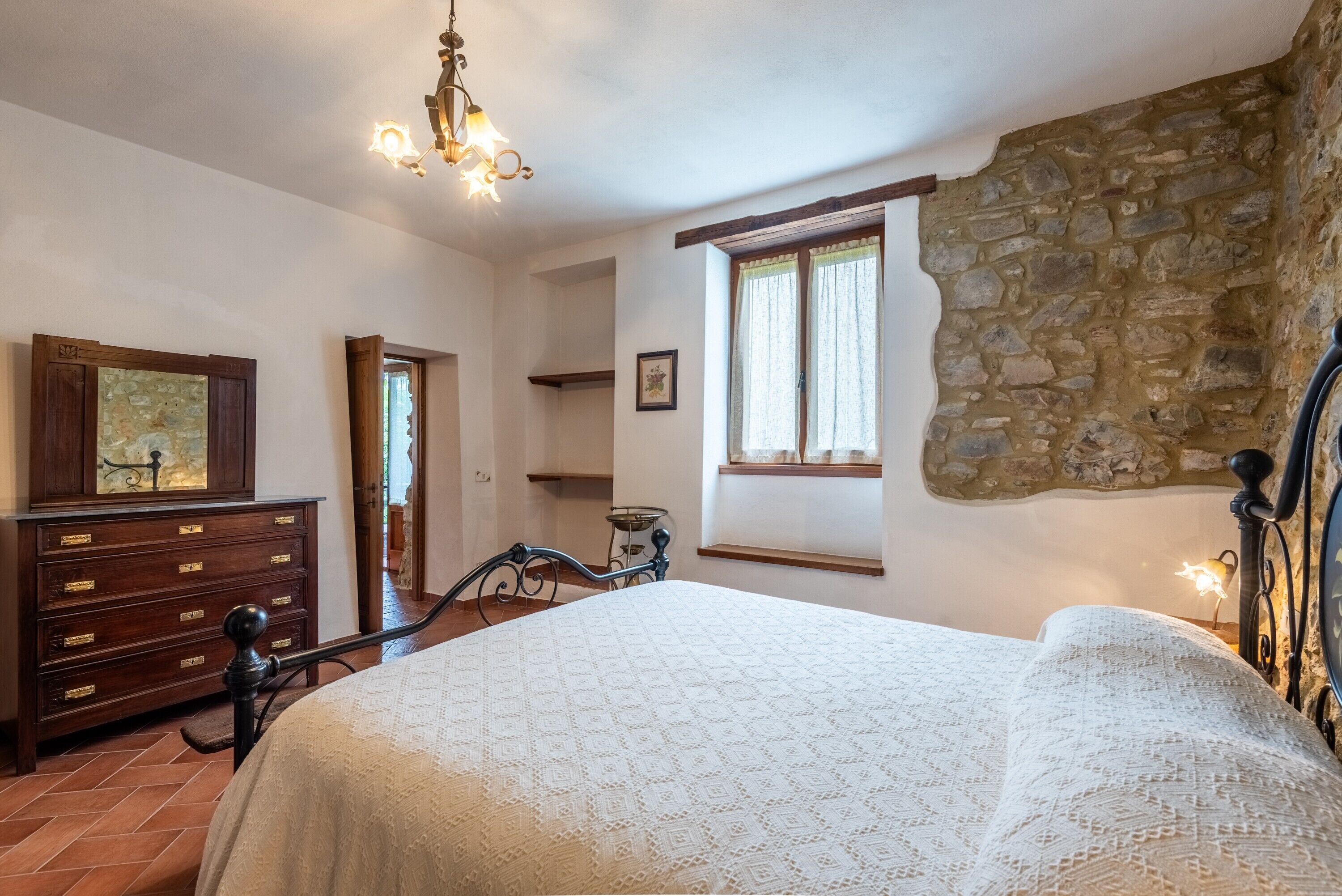 Ein Schlafzimmer mit Bett, Kommode, Steinwand, Fenster und einer Chandelier.