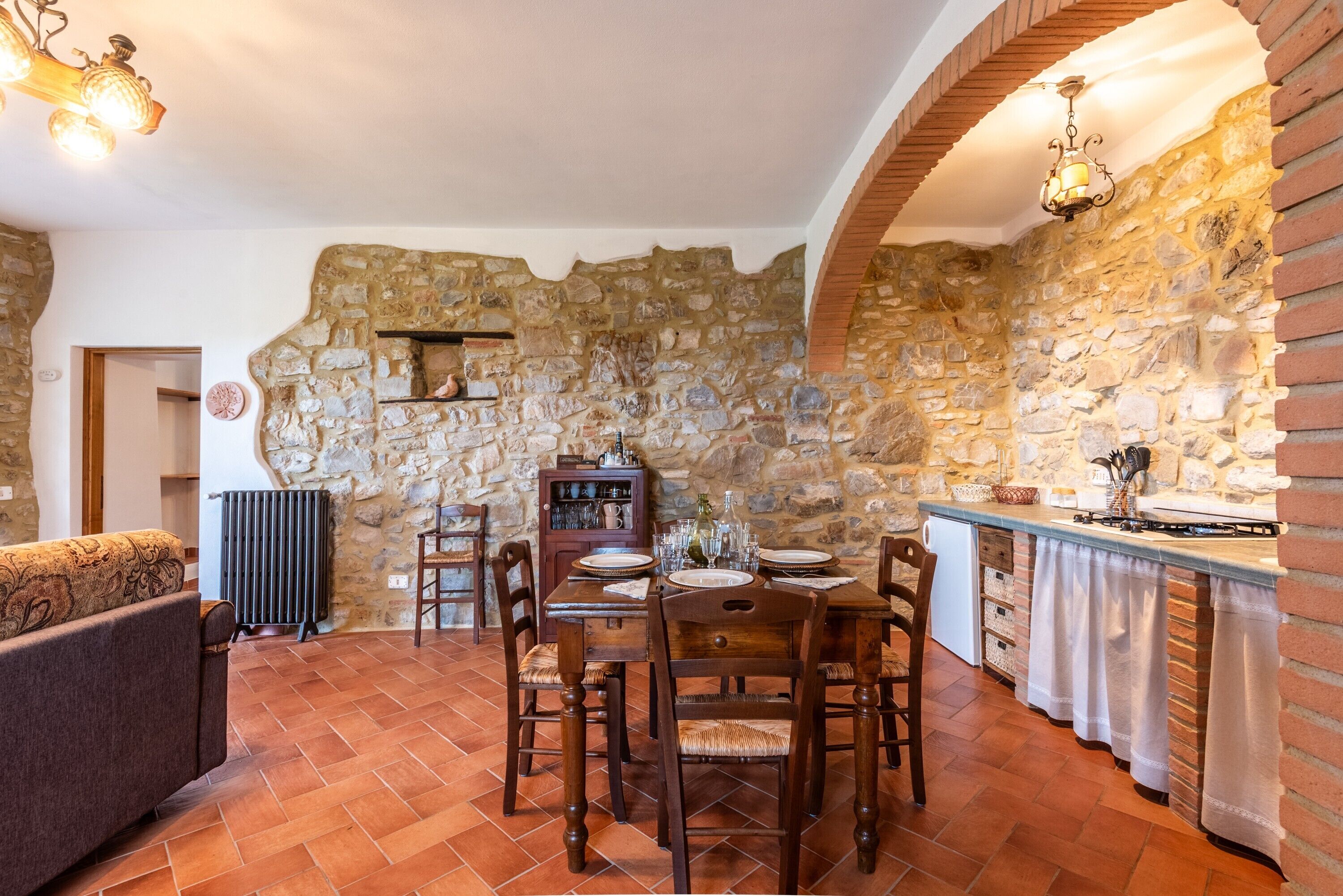A dining area with a stone wall, wooden table, chairs, and a kitchen counter.