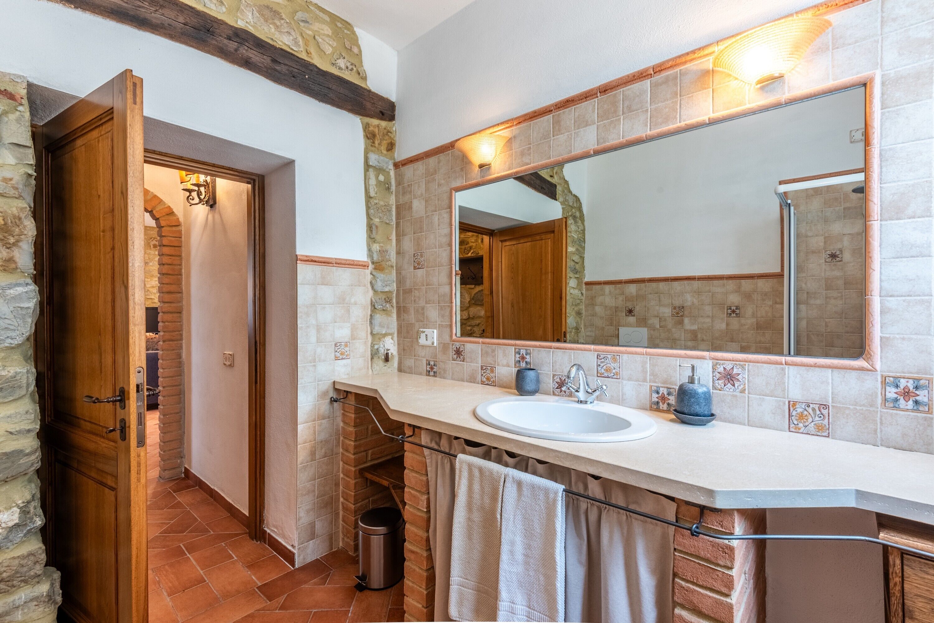 A bathroom with a stone wall, a wooden door, a large mirror, a sink, and a towel rack.