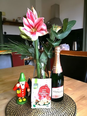 Pöydällä on viinipullo, koristeellinen kukka, pieni koriste-esine ja keksejä sisältävä pakkaus.