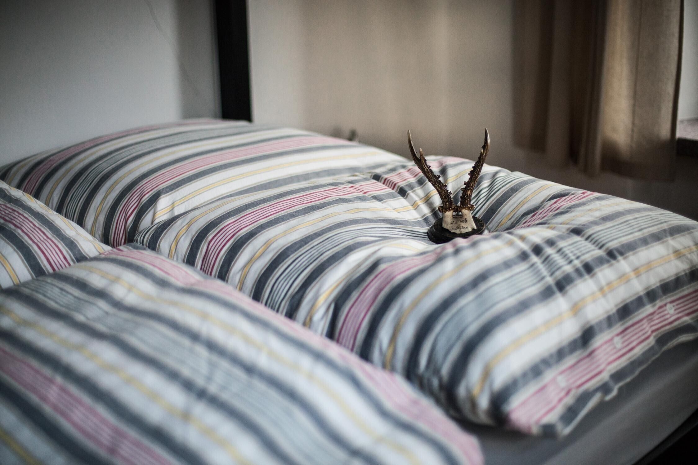 Een bed met gestreepte beddengoed en een decoratieve gewei-hoofddeksel.