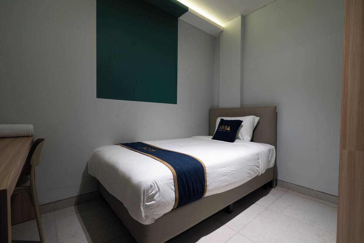 A modern hotel room with a single bed, a desk, and a teal accent wall.