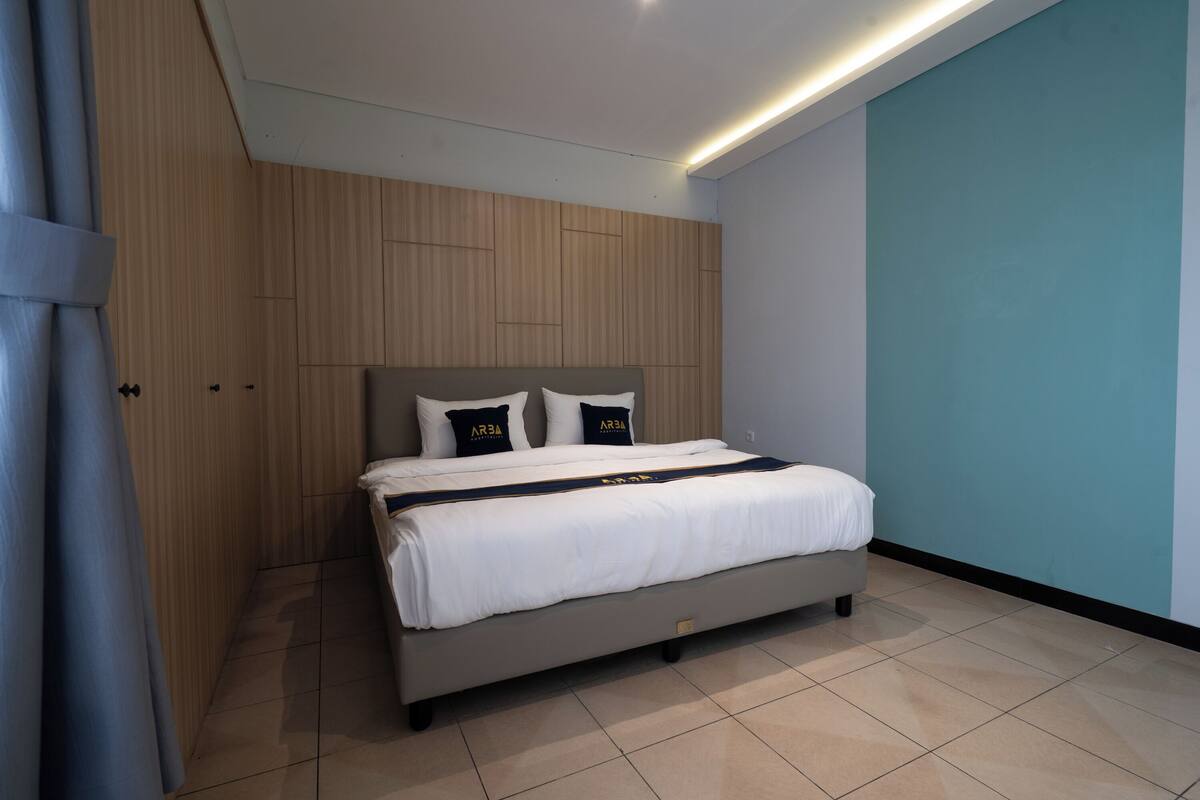 A modern bedroom with a bed, wooden panel walls, a teal accent wall, and a ceiling light.