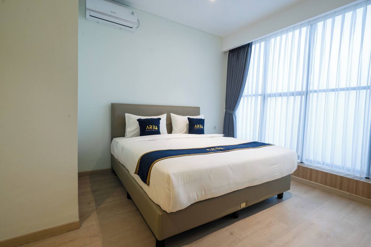 A hotel room with a large bed, a headboard, and a window with curtains.